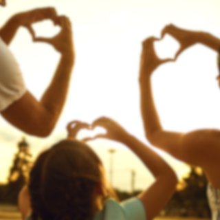 Ein Kind und seine Eltern von hinten fotografiert, sie machen alle das Herz Zeichen mit den Händen.