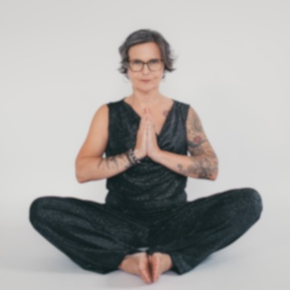 Inga Wiegert sitzt im Schneidersitz auf dem Boden, die Hände vor dem Herzen in Gebetshaltung.