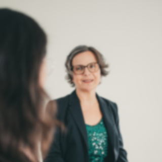 inga im grünen Pallietten Oberteil mit Blazer im Gespräch mit langhaariger Frau, die man nur von hinten sieht.