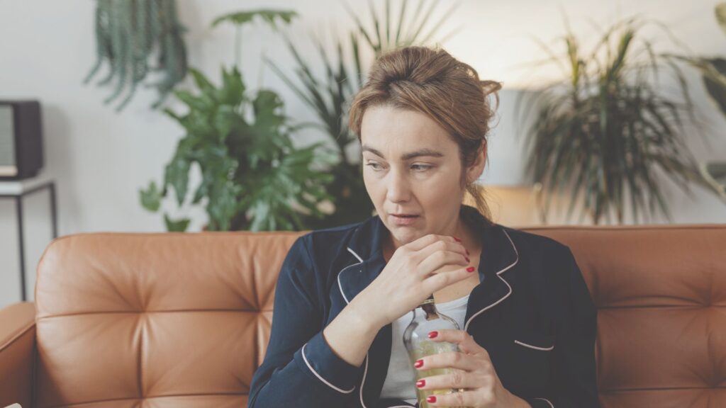 Frau sitzt auf einer brauchen Couch, sie hat eine Flasche Alkohol in der Hand.
